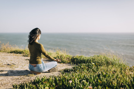 Serene woman meditating on sunny cliff overlooking sea