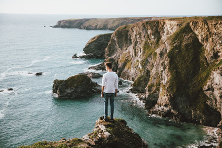 Man standing at edge of cliff over scenic ocean UK