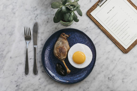 Confit duck leg and fried duck egg on restaurant table