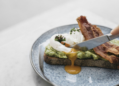Knife cutting through avocado toast with egg and bacon