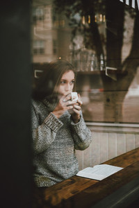 Young woman drinking coffee and reading book at cafe