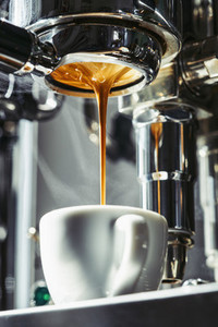 Espresso dripping from stainless steel portafilter into coffee cup