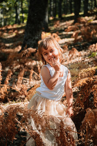 Little caucasian baby girl squatting in the forest among ferns