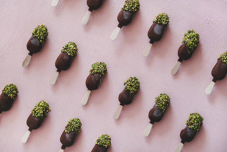 Chocolate glazed popsicle ice cream with pistachio icing over pink background