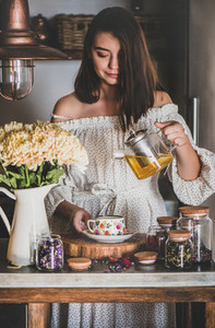 Young smiling woman pouring tea from glass pot into cup