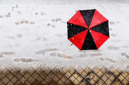Woman holding a black and red umbrella under snow