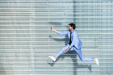 Man wearing a suit makes a selfie with a smartphone while jumping