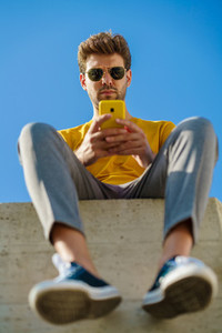 Young man using his smartphone sitting on a ledge outside