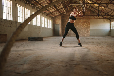 Woman doing battling rope workout in old warehouse