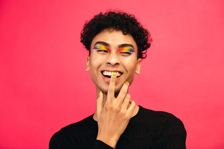 Smiling gay man with rainbow eye shadow and smiley nailpaint