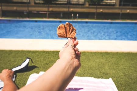Hand holding a dry leaf near a swimming pool