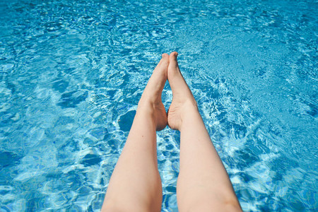White woman legs against a turquoise pool water