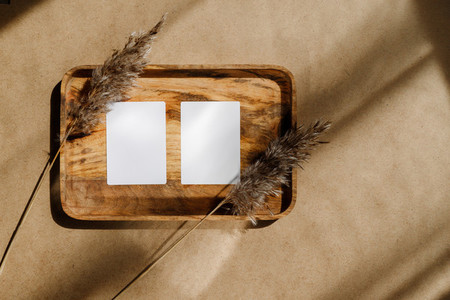 Top view of two blank paper sheet cards on a wooden tray with dry grass Beige or sand tones Mockup for business template copy space