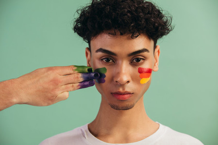 Man getting gay pride flag painted on his face