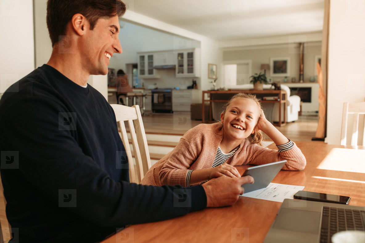 Smiling father and daughter at home with digital tablet