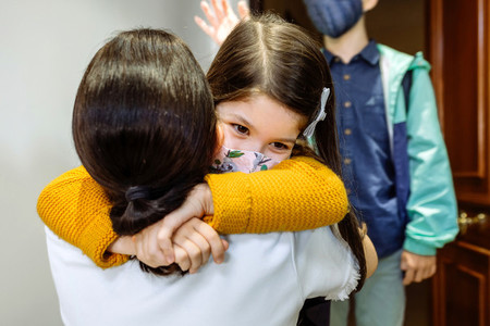 Mother hugging daughter with mask coming back from school