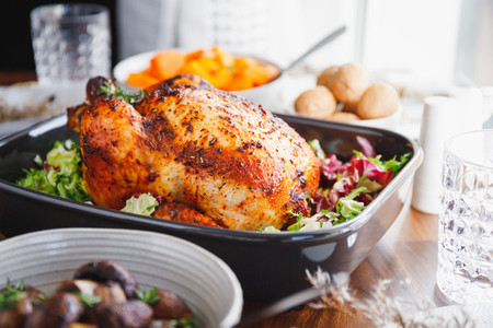 Whole roasted chicken served with fresh salad in black pan on a festive table  Thanksgiving or family dinner celebration cooking concept