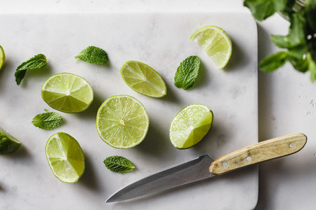 Cutted fresh lime on a white marble kitchen board with mint  Preparation beverage or food cooking concept