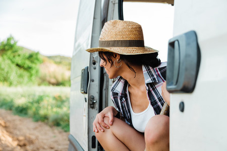 Young farmer woman resting in a van at crop field