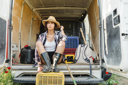 Young farmer woman resting in a van at crop field