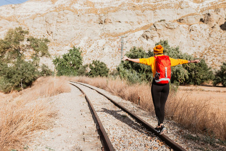 Back view of professional female hiker with tourist backpack exploring wilderness environment during hiking trekking on railway