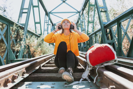 Woman listening to music with her headphones on an abandoned railway bridge