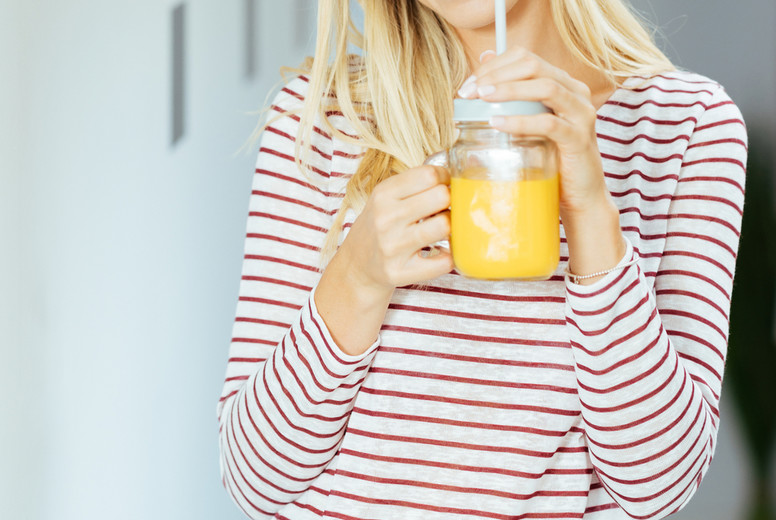 Smiling woman drinking a glass of natural orange juice at home.