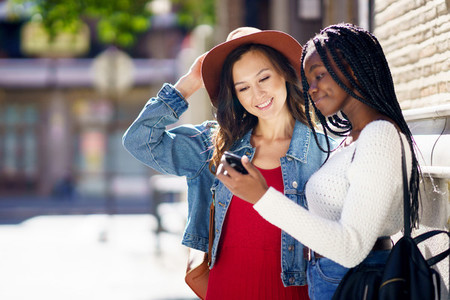 Two friends looking at their smartphone together  Multiethnic women