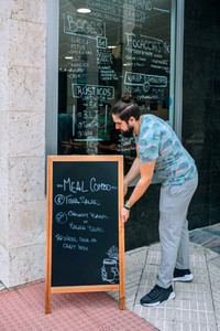 Young waiter placing a blackboard with the daily menu outdoors
