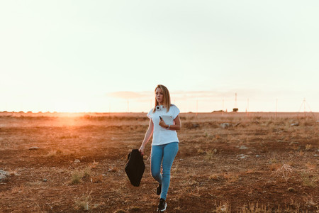 Young woman walking through the field with her laptop case
