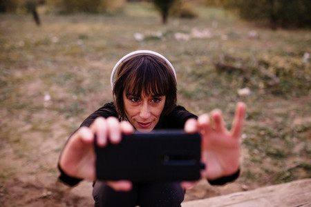 Woman in sport clothes on a wooden bench taking a selfie