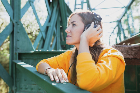Woman listening to music with her old headphones on an abandoned iron bridge