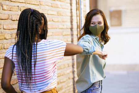 Multiethnic young women wearing masks greeting at each other with their elbows
