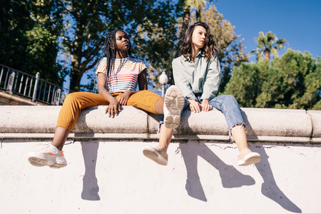 Two multiethnic women sitting on a urban wall