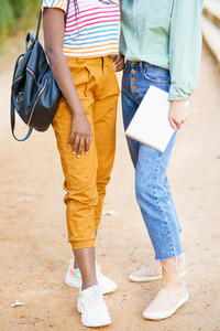Two unrecognizable multiethnic girls posing together with colorful casual clothing