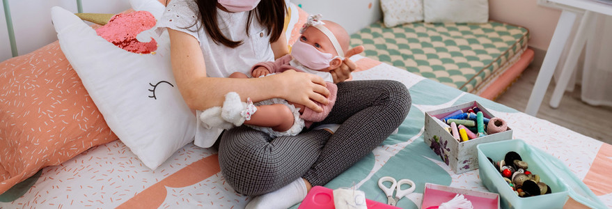 Girl with mask playing to take care of her baby doll with mask