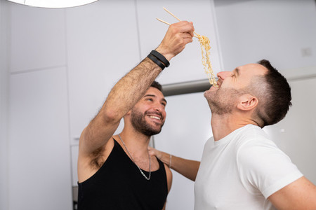 Man feeding pasta to his boyfriend in a fun way