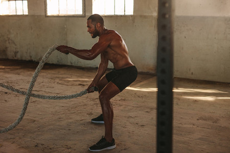Muscular man doing battle rope workout