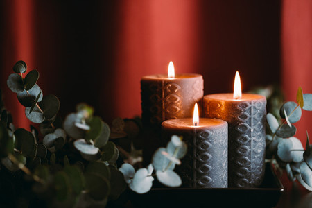 Black burning candles against dark red background with eucalyptus branch