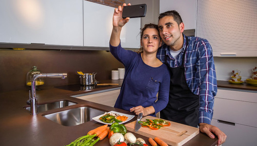 Couple in kitchen cooking and taking selfie with smartphone