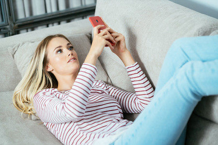 Young caucasian woman using her smartphone lying on the sofa