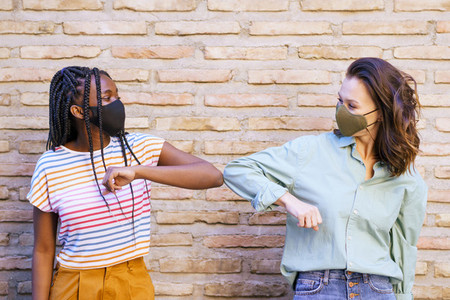 Multiethnic young women wearing masks greeting at each other with their elbows