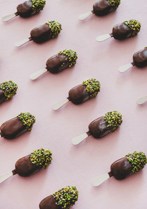 Chocolate glazed ice cream pops with pistachio icing over pink background