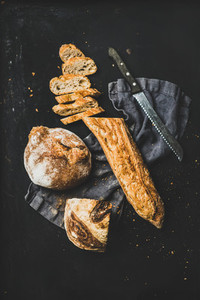 Flat lay of baguette in slices and loaf over black background