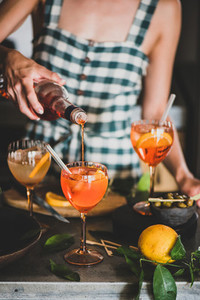 Young woman pouring aperol liquor to alcohol cocktail spritz