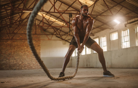 Strong and masculine athlete working out with battle rope