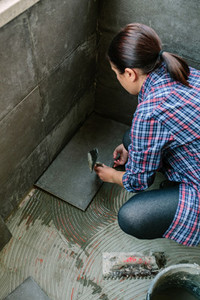 Female manual worker laying a new tile floor