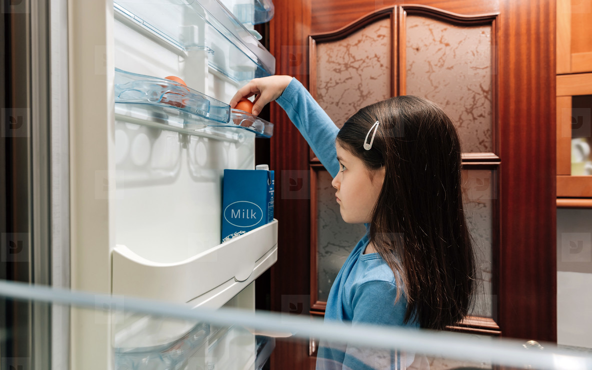 Sad girl taking an egg from the empty fridge