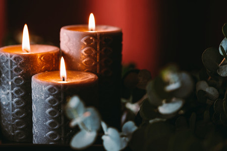 Black burning candles against dark red background with eucalyptus branch