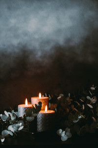 Black burning candles against dark background with eucalyptus branch